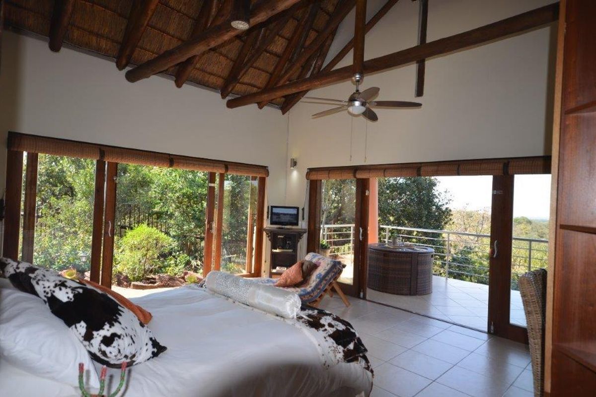 Spacious bedroom featuring a high thatched ceiling with exposed timber trusses, tiled floors, and large sliding glass doors opening onto a private balcony.