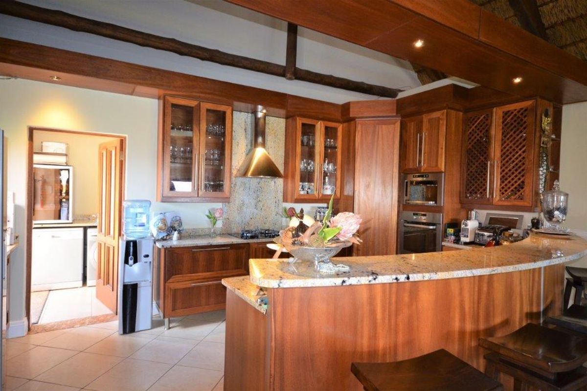 A well-appointed kitchen featuring warm wooden cabinetry, granite countertops, integrated appliances, and exposed timber beams, with an adjacent scullery area.