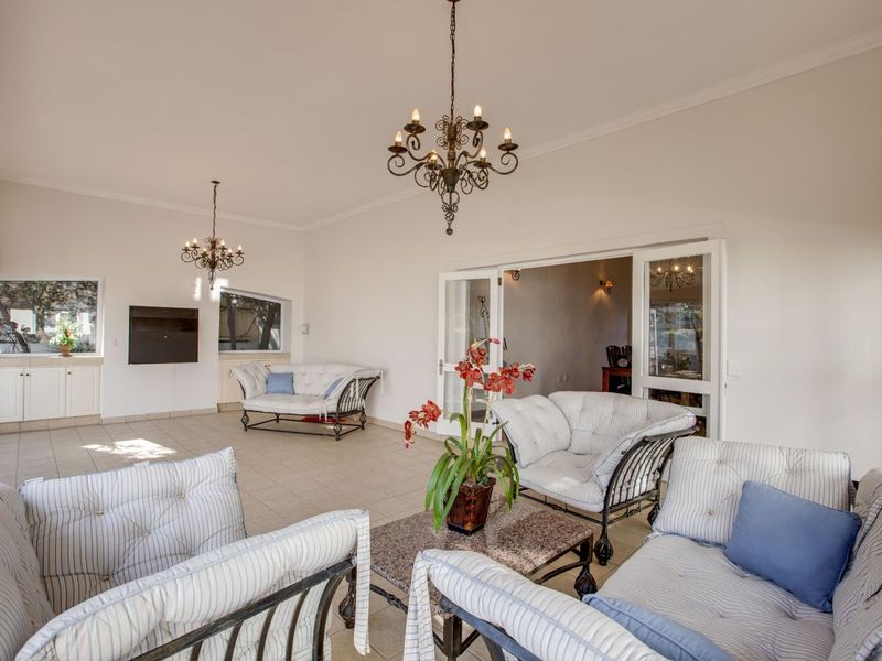 Spacious living area featuring tiled flooring, elegant chandeliers, and double glass doors leading to an adjacent room, offering a bright and airy atmosphere.