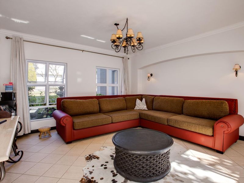 A bright and spacious living room featuring tiled flooring, crown molding, and elegant lighting fixtures, including a central chandelier and wall sconces.