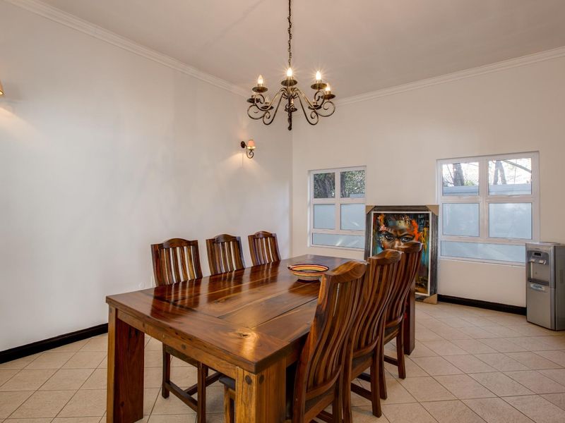 A well-lit dining room featuring tiled flooring, classic wrought iron chandelier lighting, and large windows providing natural light.