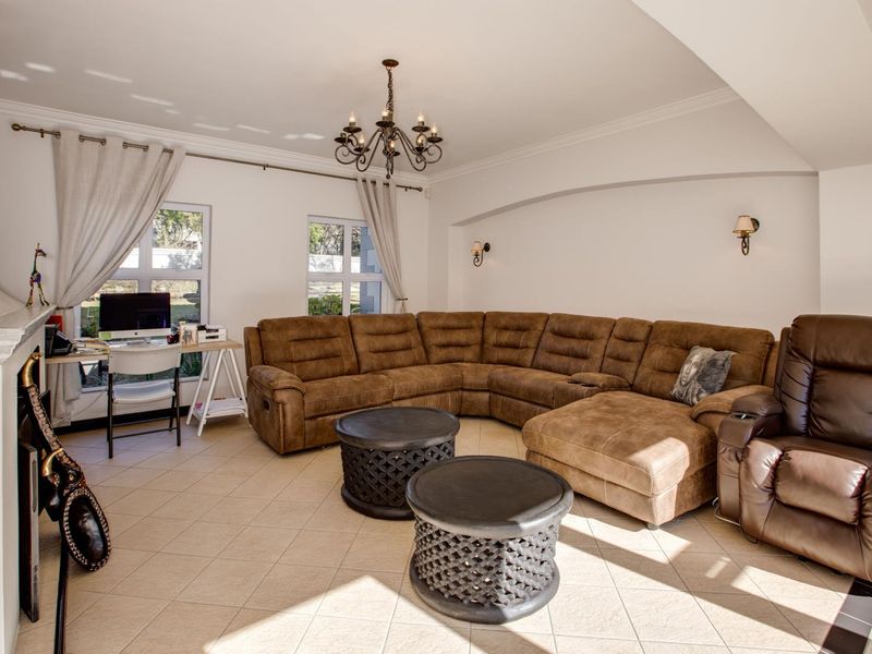 Spacious living room featuring tiled flooring, a fireplace, elegant crown molding, and a classic chandelier, creating a warm and inviting atmosphere.