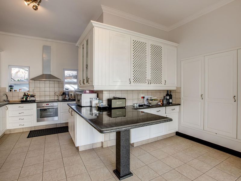 A functional kitchen featuring white cabinetry, granite countertops, a breakfast bar, built-in oven, and extractor fan with tiled flooring and backsplash.