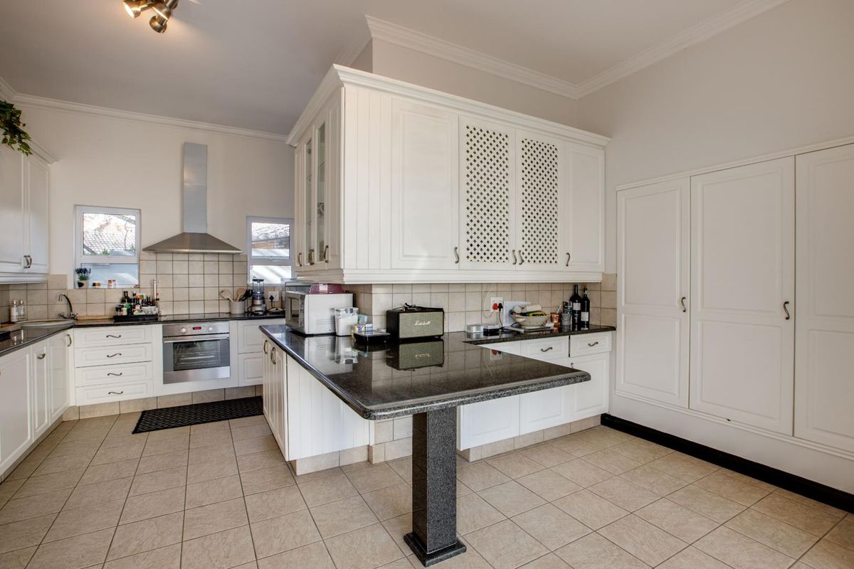 A functional kitchen featuring white cabinetry, granite countertops, a breakfast bar, built-in oven, and extractor fan with tiled flooring and backsplash.