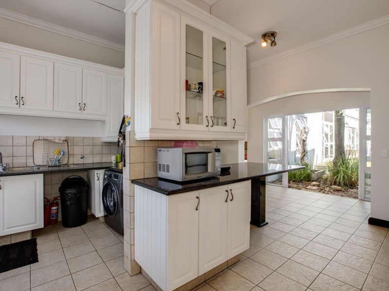 A functional kitchen featuring white cabinetry, granite countertops, tiled flooring, and an open-plan layout leading to an outdoor patio area.