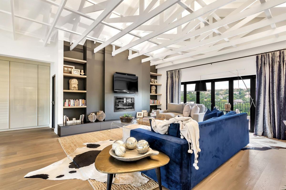 Spacious living room featuring high vaulted ceilings with exposed white beams, a modern fireplace, built-in shelving, and large glass doors opening to a balcony.