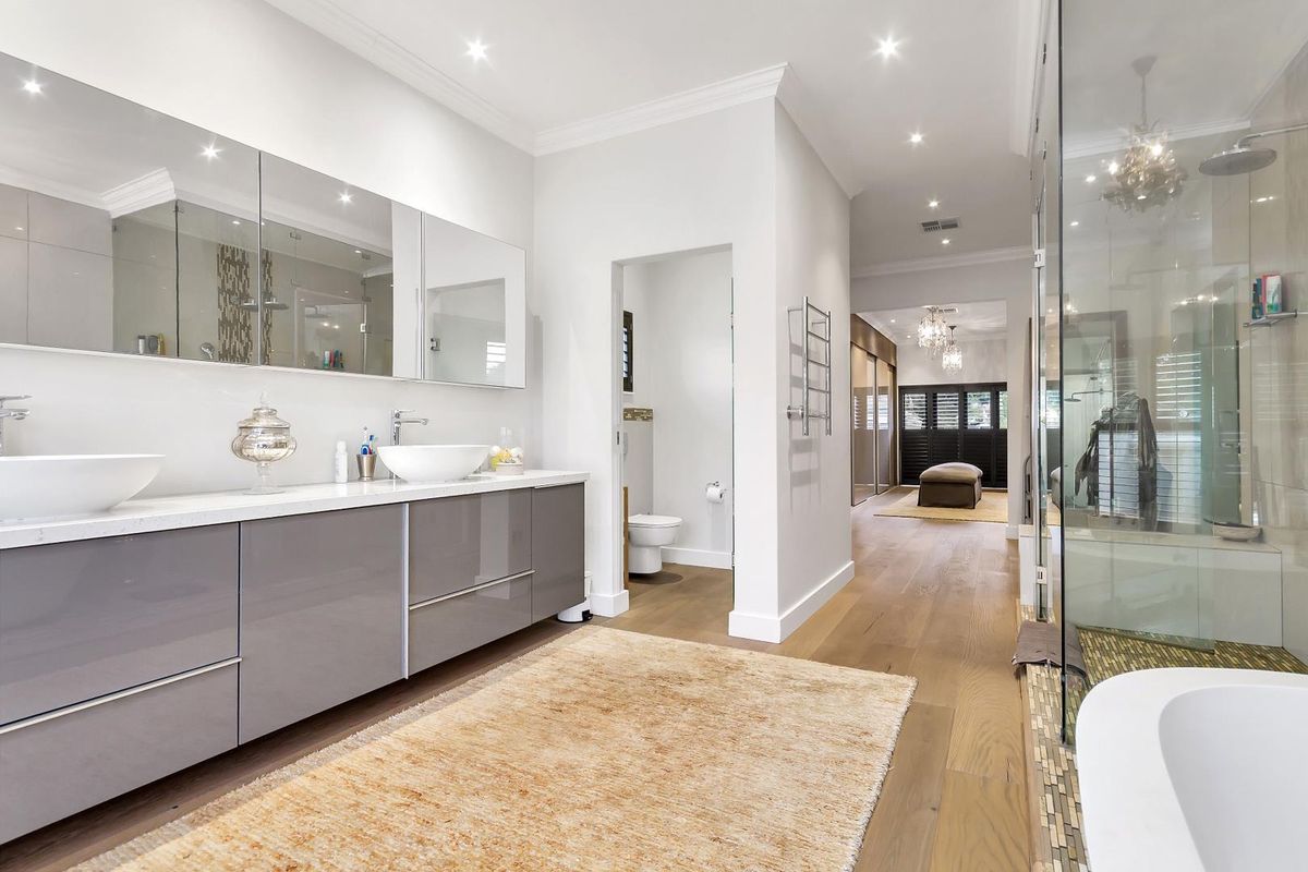 Modern bathroom featuring a double vanity with vessel sinks, a glass-enclosed shower, a separate toilet area, and high-quality timber flooring.