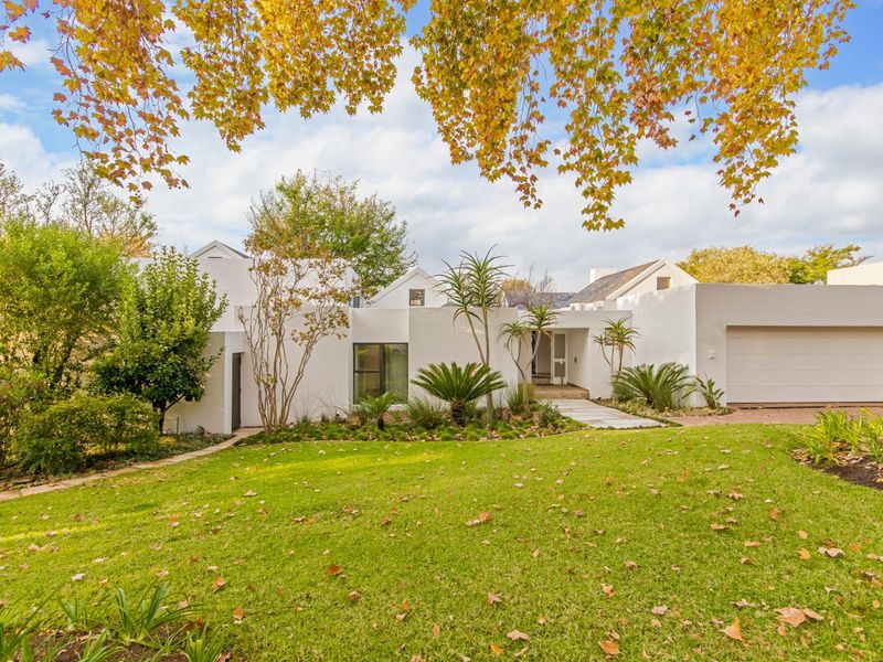 A well-maintained front elevation of a white house featuring a landscaped garden, paved walkway, and an integrated garage.