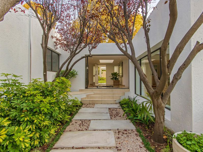 A beautifully landscaped rear courtyard featuring a paved walkway leading to a modern entrance with large sliding glass doors and a skylight.