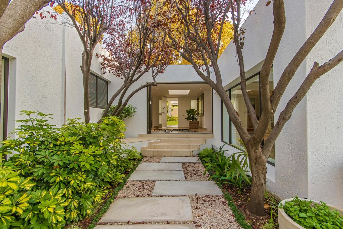 A beautifully landscaped rear courtyard featuring a paved walkway leading to a modern entrance with large sliding glass doors and a skylight.