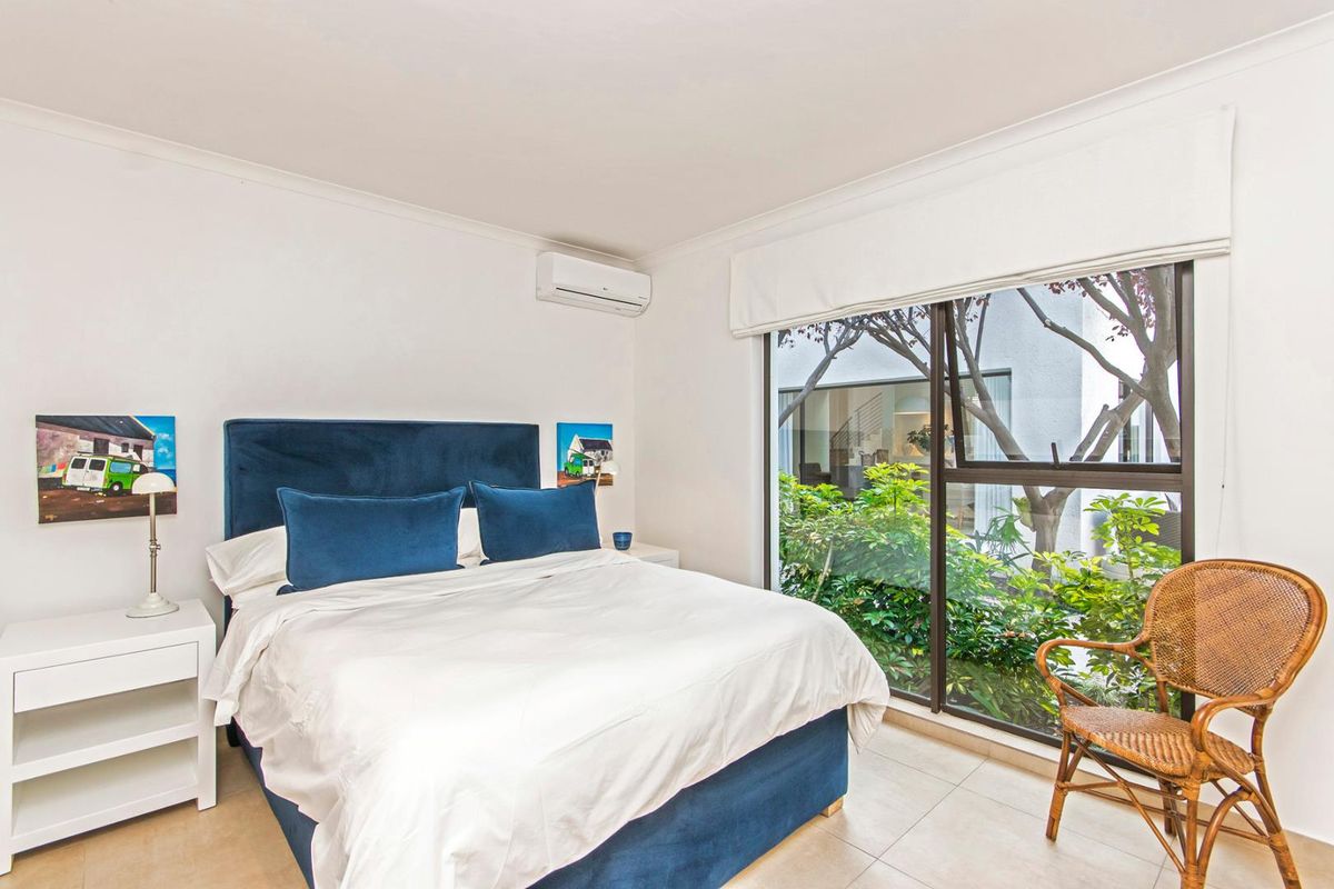 A bright bedroom featuring tiled flooring, a split-system air conditioner, and a large sliding glass door providing views of the garden.