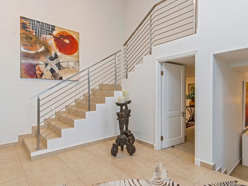 A bright entrance hall featuring a modern staircase with stainless steel balustrades and neutral tiled flooring.