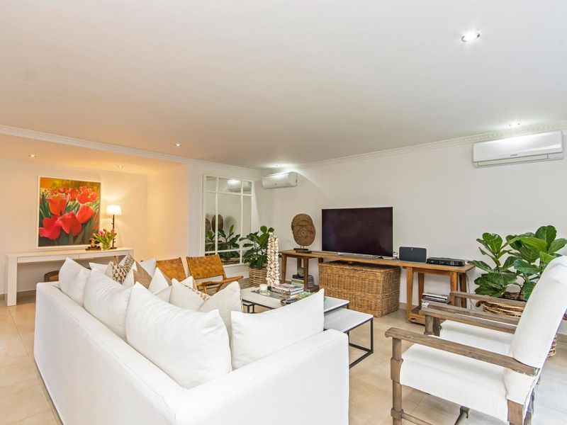 A bright and spacious living room featuring tiled flooring, recessed downlighting, crown molding, and dual split-system air conditioning units.