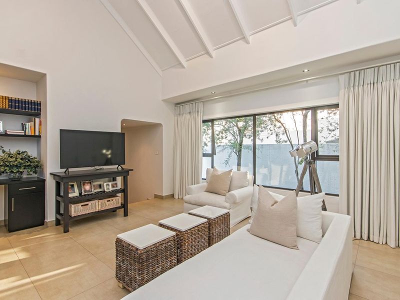 Spacious living room featuring a high vaulted ceiling with exposed rafters, tiled flooring, built-in shelving, and large windows providing ample natural light.