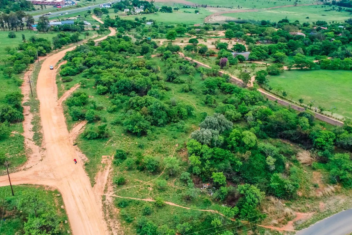 Aerial view of a large, undeveloped commercial land parcel featuring natural vegetation, a dirt access road, and perimeter boundary walls.