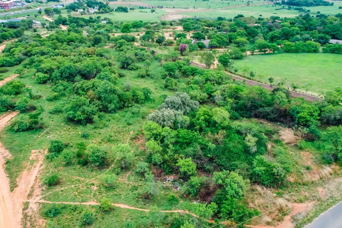 Aerial view of a large, undeveloped commercial land plot featuring dense vegetation, bordering both dirt and paved road access.