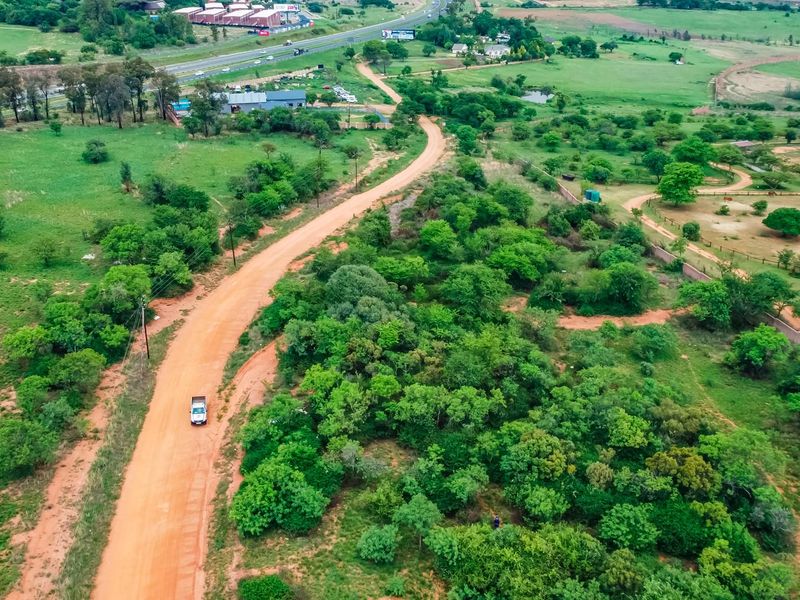 An aerial view of a large, undeveloped commercial land plot featuring natural vegetation and an access dirt road.