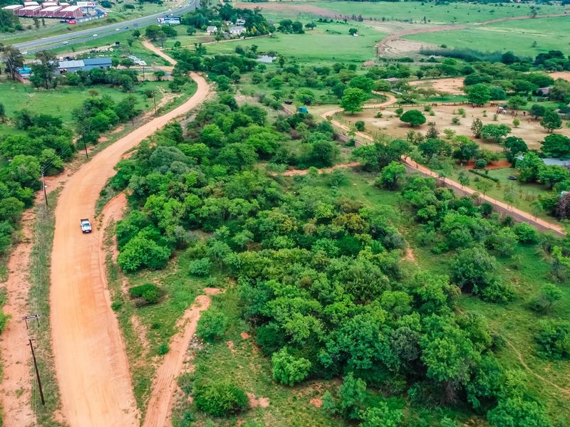 An aerial view of a large vacant commercial land plot featuring natural vegetation, trees, and an unpaved access road.