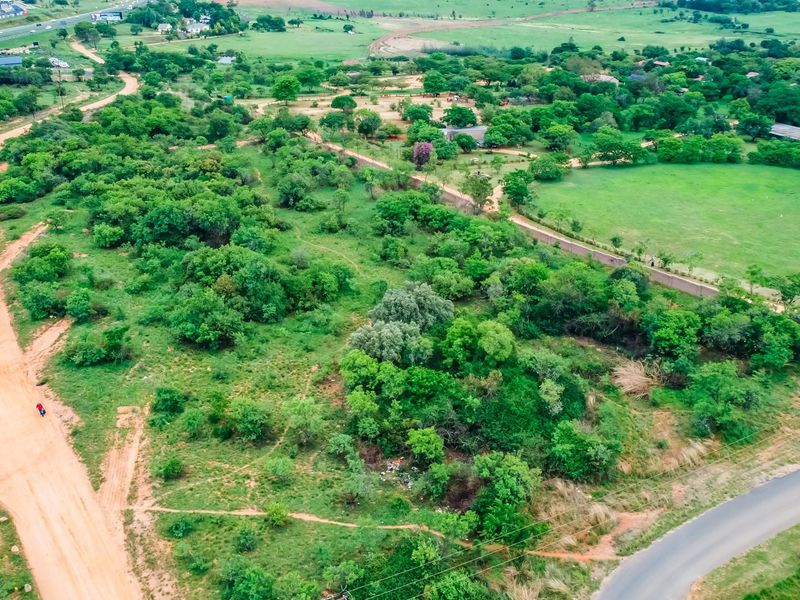 Aerial view of a large vacant commercial land plot featuring natural vegetation, bordering both dirt and paved road access.