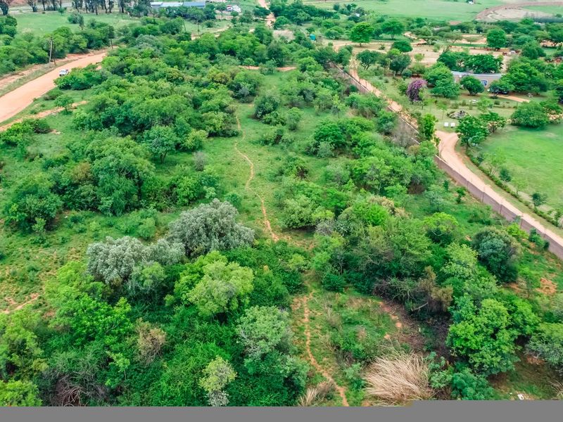 Aerial view of a large, undeveloped commercial land parcel featuring natural vegetation, perimeter fencing, and access via a dirt road.