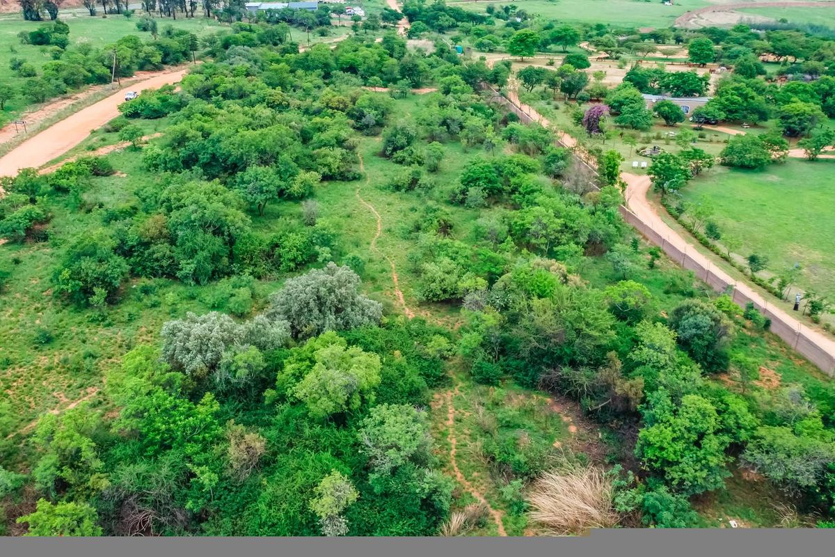 Aerial view of a large, undeveloped commercial land parcel featuring natural vegetation, perimeter fencing, and access via a dirt road.