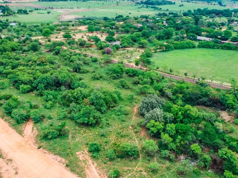 An aerial view of a large, undeveloped commercial land parcel featuring mature vegetation, dirt road access, and established perimeter boundary walls.