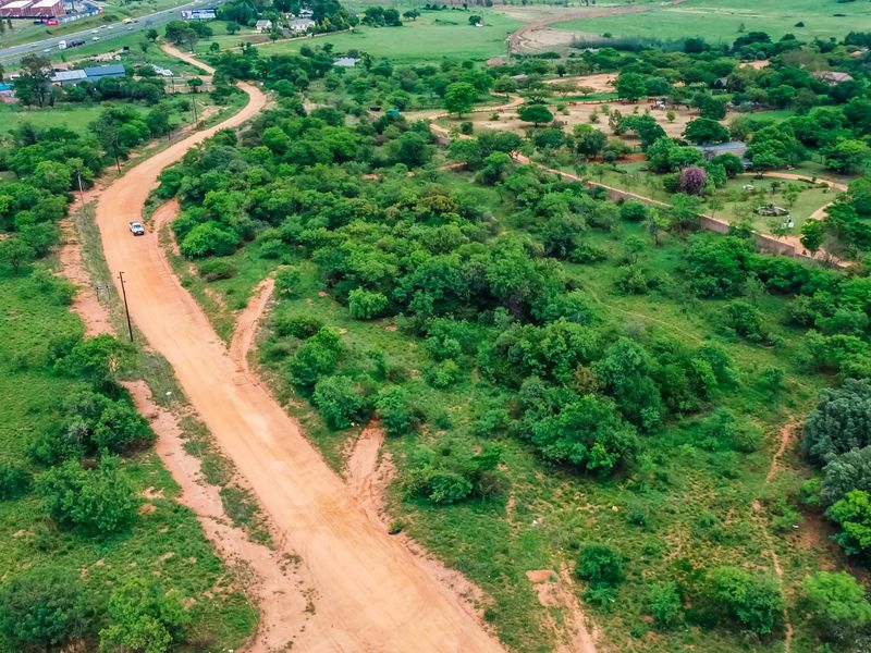 An aerial view of a large, undeveloped commercial land parcel featuring natural vegetation and an unpaved access road.