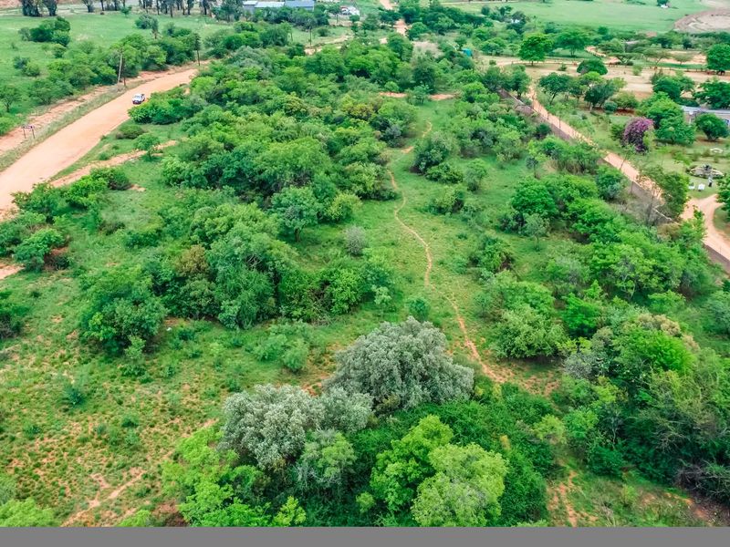 An aerial view of a vacant commercial land plot featuring natural vegetation, surrounding dirt roads, and established boundary fencing.