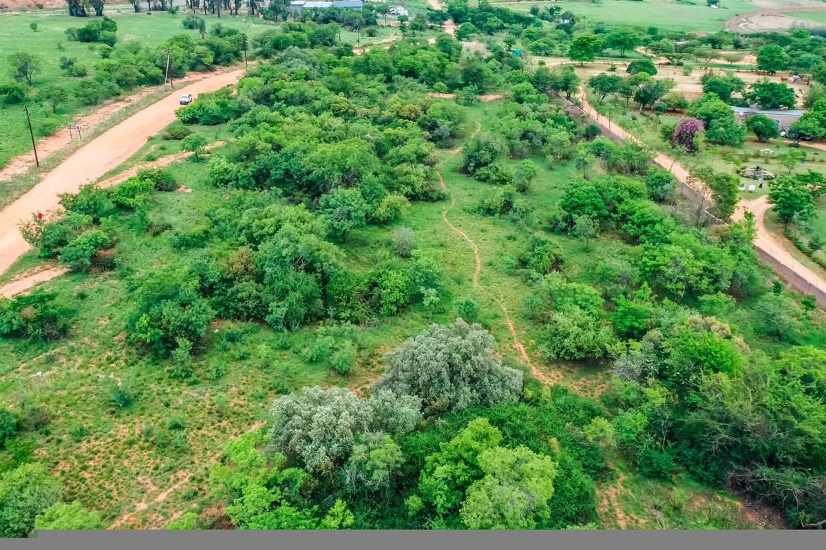 An aerial view of a vacant commercial land plot featuring natural vegetation, surrounding dirt roads, and established boundary fencing.