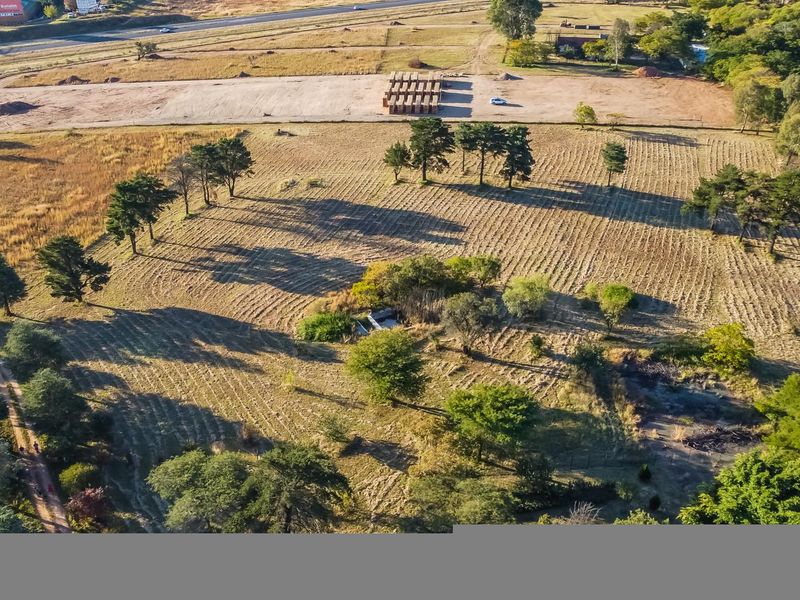 An aerial view of a large, open farm plot featuring established trees, internal dirt tracks, and perimeter fencing, situated near a main road.