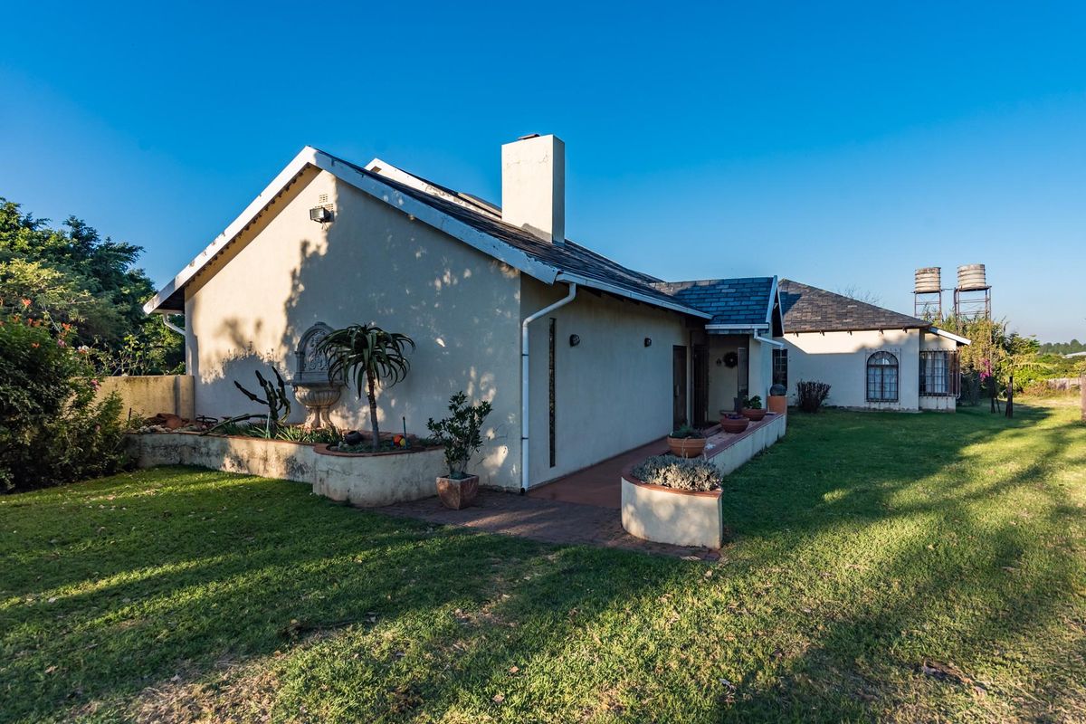 Rear view of the farmhouse featuring a slate roof, chimney, paved walkway, and elevated water tanks set within a spacious garden.