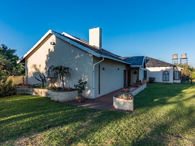 Rear view of the farmhouse featuring a slate roof, chimney, paved walkway, and elevated water tanks set within a spacious garden.