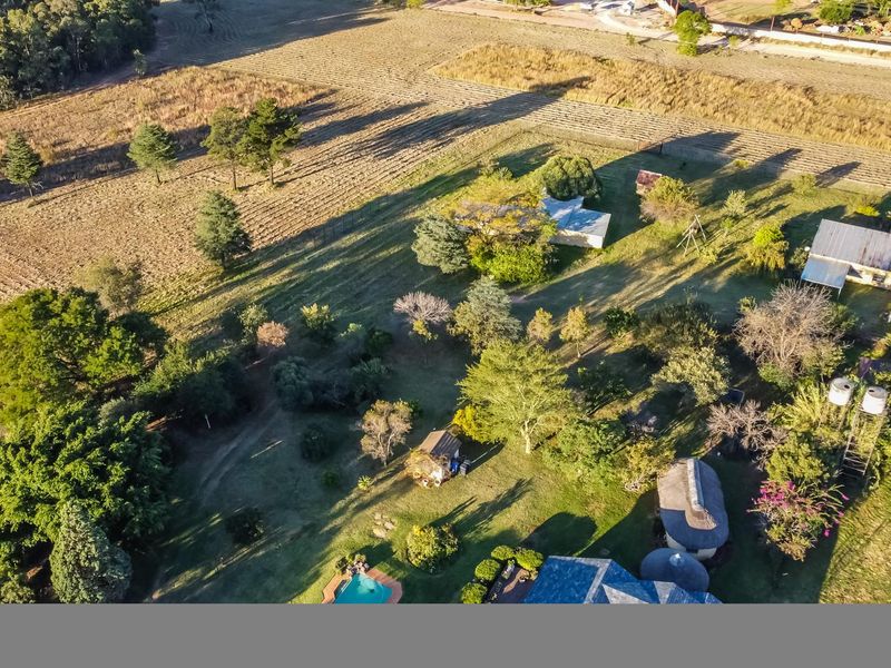 Aerial view of a farm property featuring multiple structures, a swimming pool, water tanks, and extensive landscaped grounds.