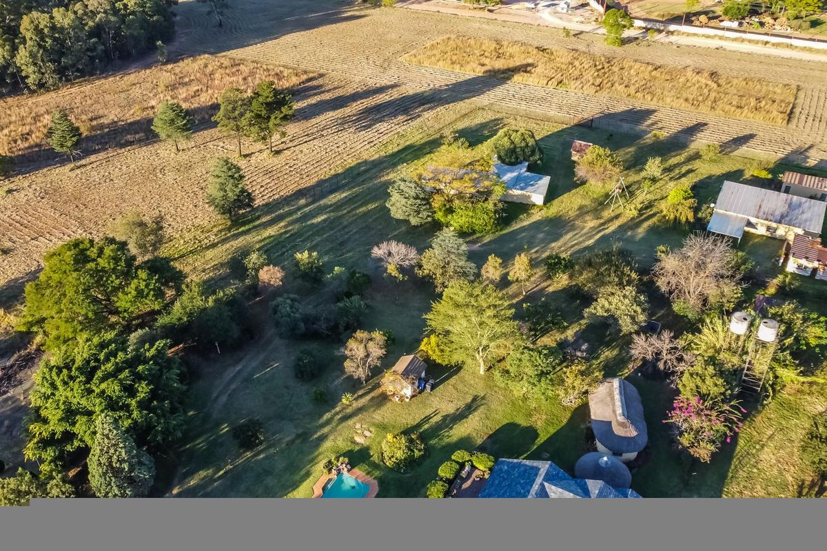 Aerial view of a farm property featuring multiple structures, a swimming pool, water tanks, and extensive landscaped grounds.