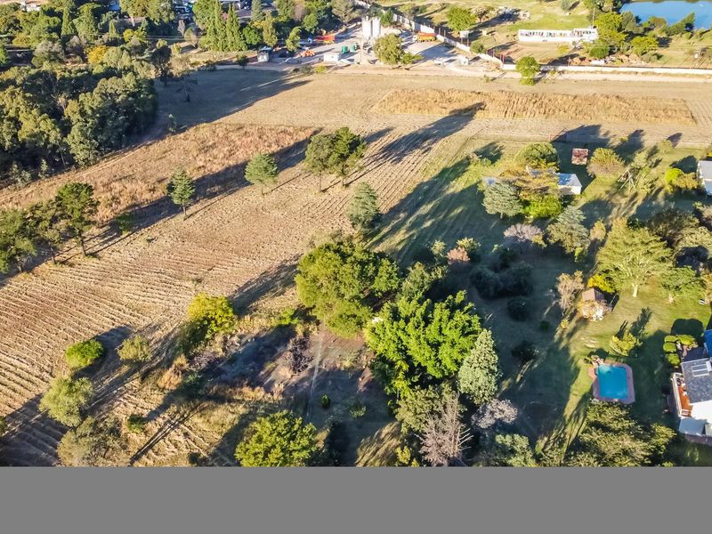 Aerial view of a farm property featuring a swimming pool, established garden, and expansive open land with mature trees.