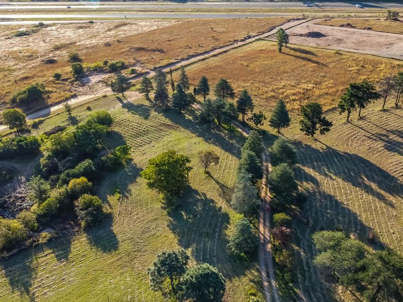 An aerial view of the farm property featuring open grassland, established trees, and a dirt access road.