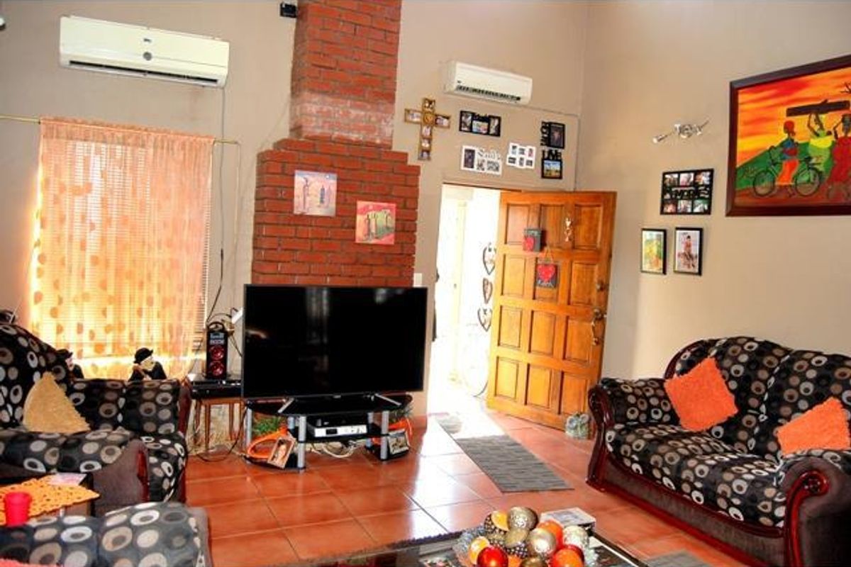 Spacious living room featuring a prominent exposed brick fireplace, tiled flooring, and dual wall-mounted air conditioning units.