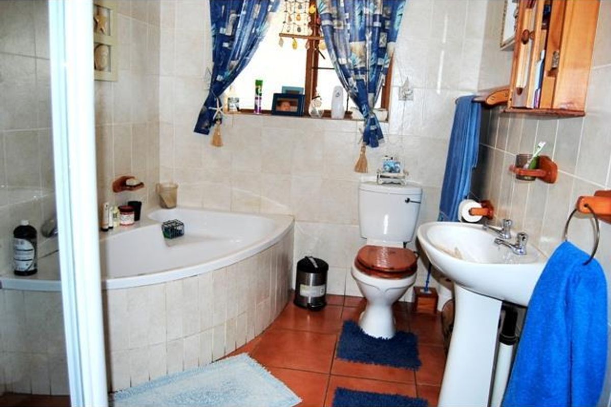 A functional bathroom featuring a corner bathtub, pedestal basin, and toilet with neutral wall tiling and terracotta floor tiles.