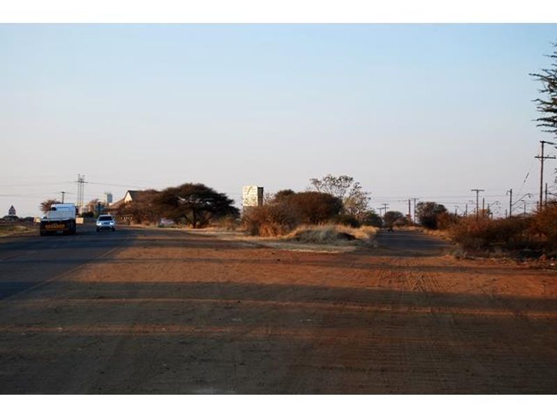 A view of an unpaved access road and surrounding vacant land with visible utility infrastructure and power lines.