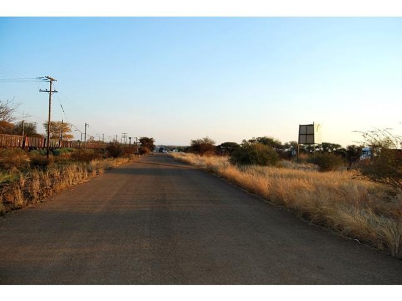 A view of an asphalt road bordered by dry vegetation, utility poles, and a large billboard structure.