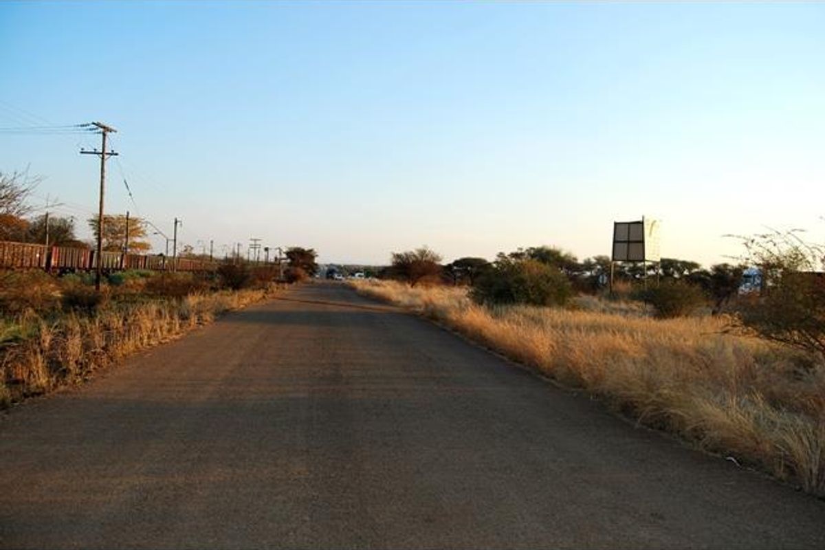 A view of an asphalt road bordered by dry vegetation, utility poles, and a large billboard structure.
