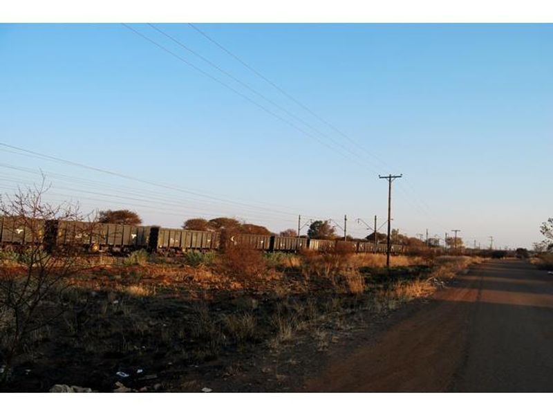 A view of the vacant commercial land adjacent to a railway line and public road, featuring overhead utility infrastructure.