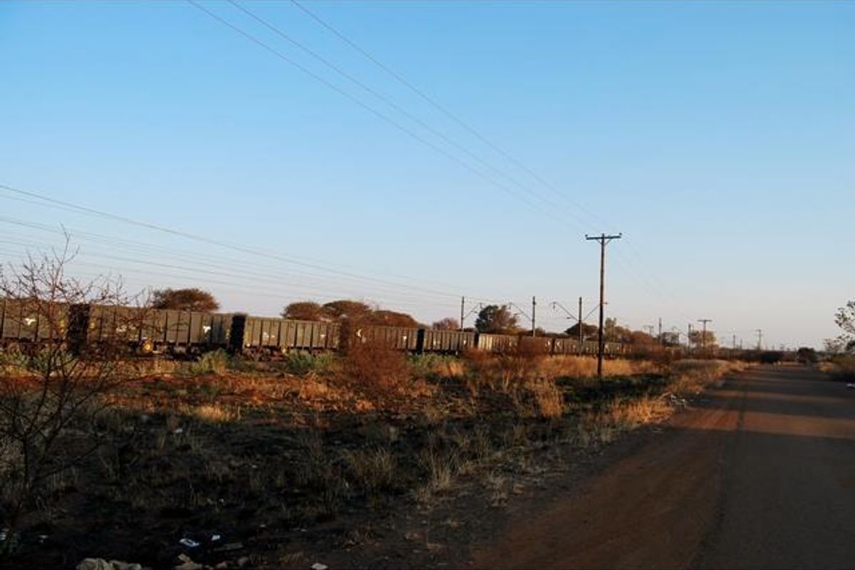 A view of the vacant commercial land adjacent to a railway line and public road, featuring overhead utility infrastructure.