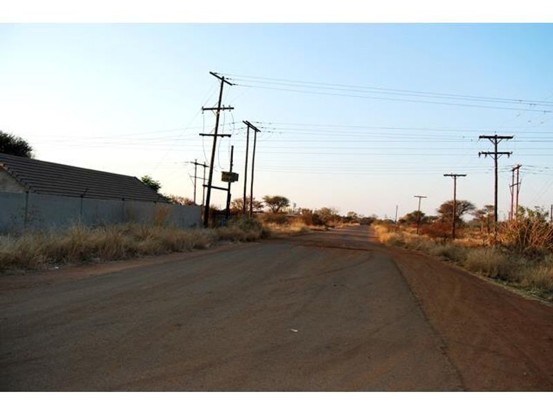 A view of an unpaved road with visible utility poles and overhead power lines, bordering a property with a perimeter wall.