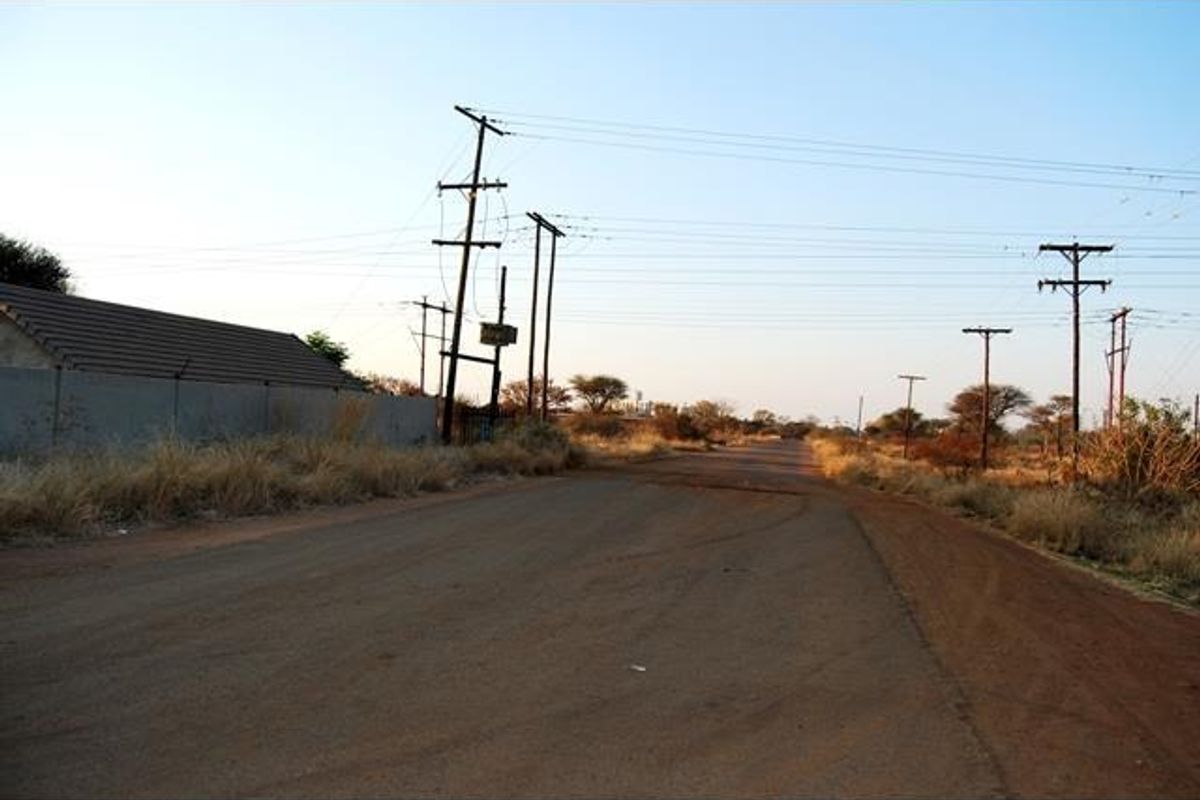 A view of an unpaved road with visible utility poles and overhead power lines, bordering a property with a perimeter wall.