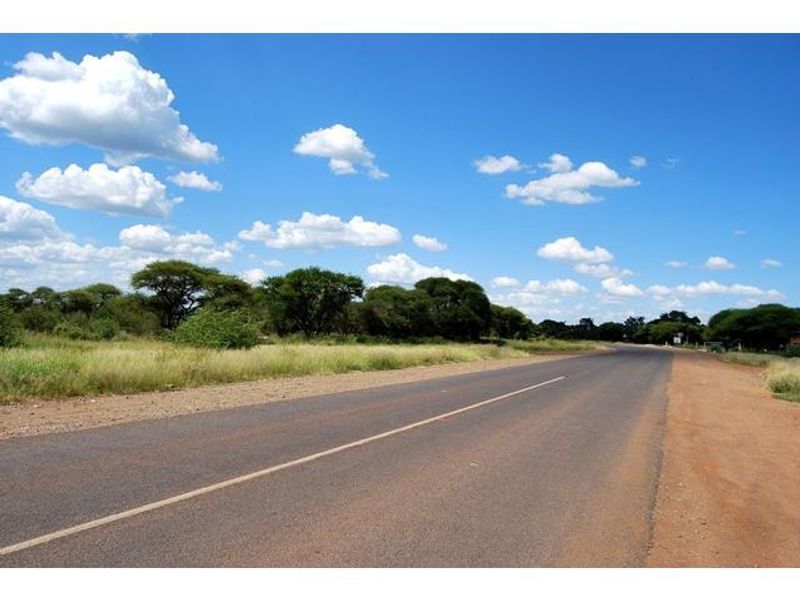 A view of the paved road leading towards the vacant residential land, featuring natural vegetation and clear skies.