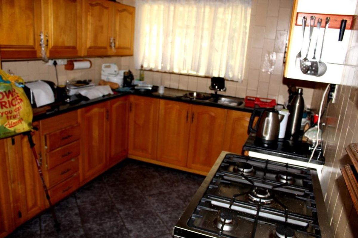 A functional kitchen featuring wooden cabinetry, a gas hob, and tiled flooring, offering a traditional layout with ample storage space.