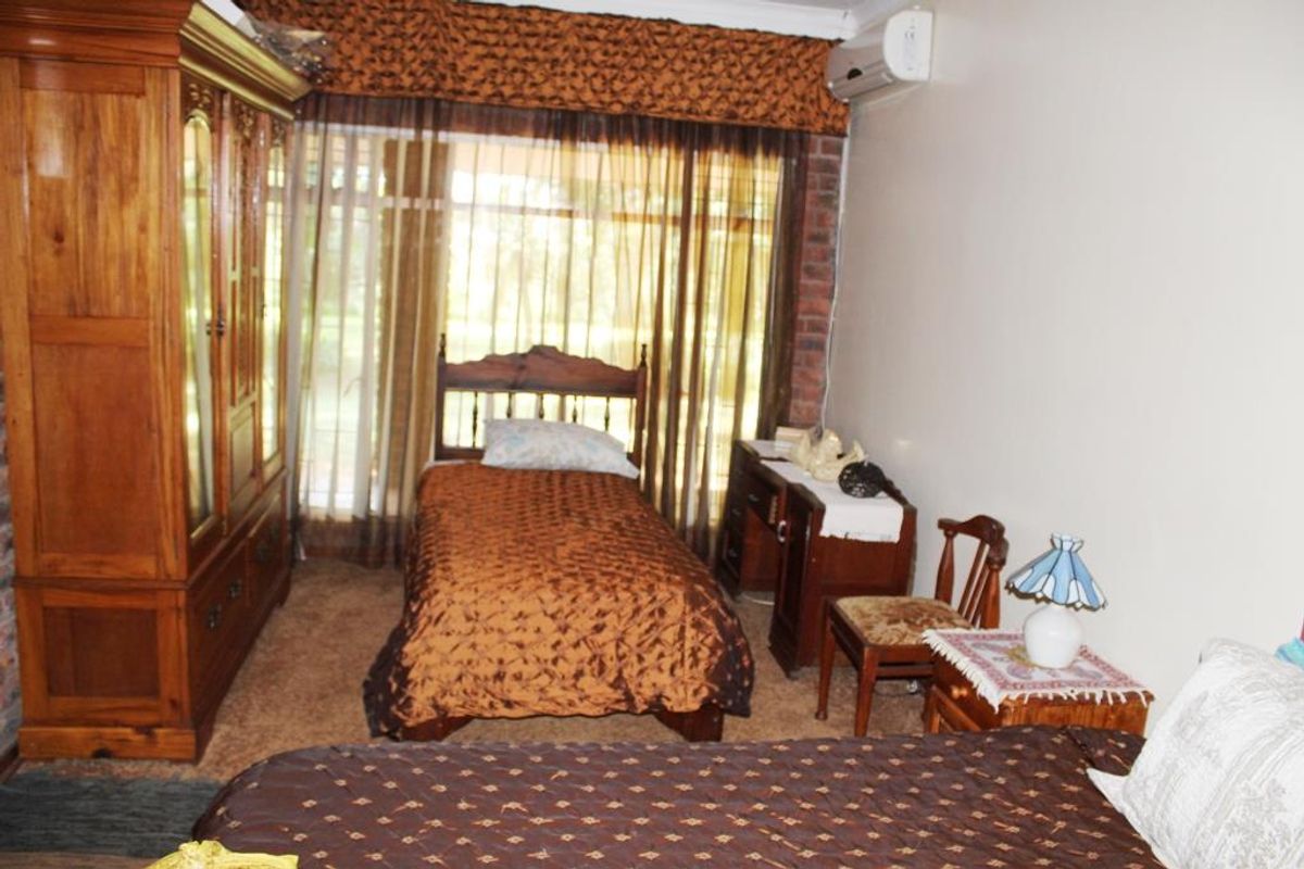 A bedroom featuring a wall-mounted air conditioning unit, exposed brick accents, and large windows with curtain pelmets.