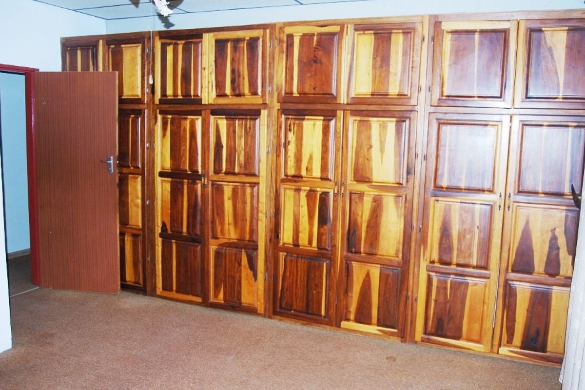 A bedroom featuring extensive floor-to-ceiling built-in wooden cabinetry providing ample storage space, complemented by carpeted flooring and a ceiling fan.