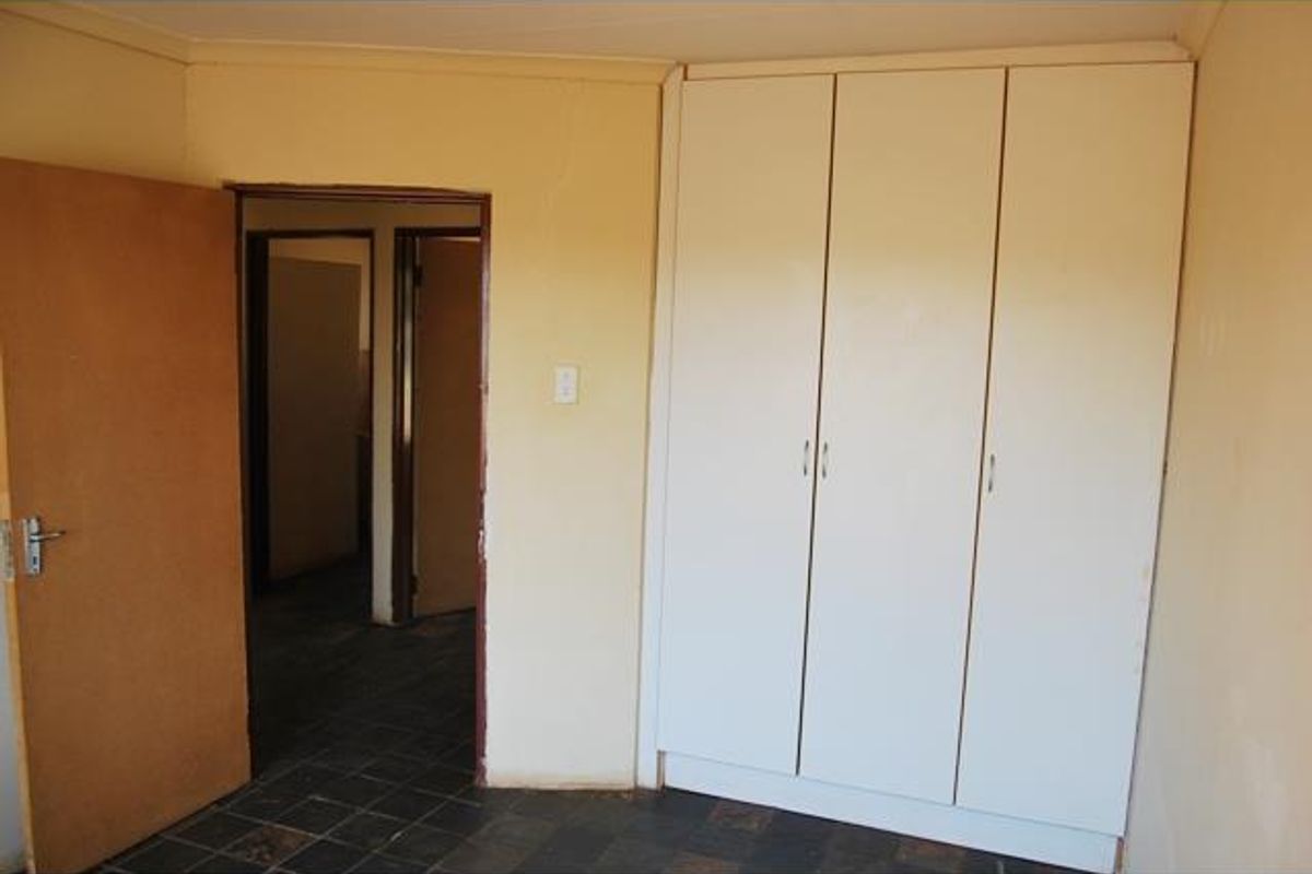 A bedroom featuring built-in cupboards, tiled flooring, and access to an adjacent hallway.